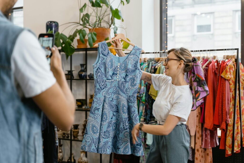 Woman happily showcasing a blue dress during a boutique sale, enhancing live shopping experience.